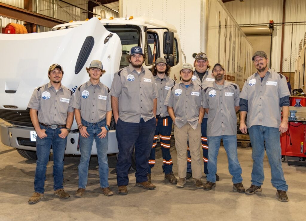 group of students standing in front of a semi truck in a repair shop.