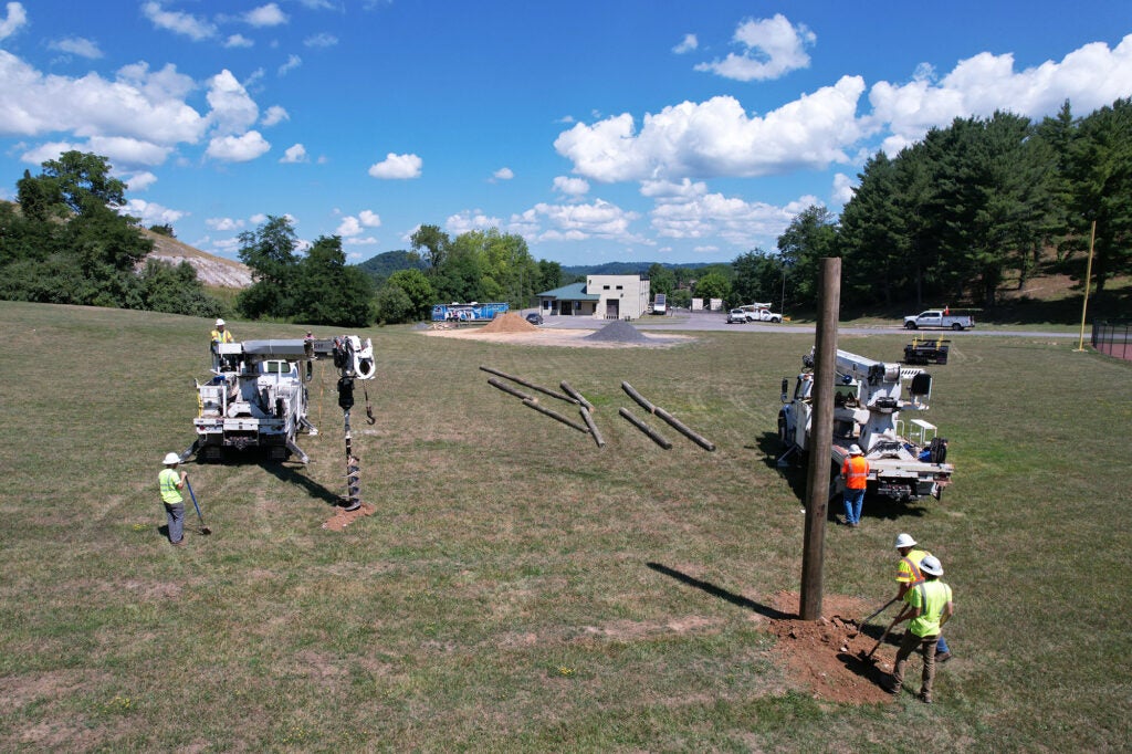 Workers install utility poles for students to learn how to work in the air