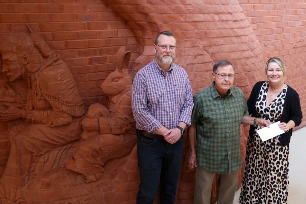 Dr. Hayes, Dr. Susan Lowe, and James Carter meeting in front of a brick masonry wall sculpture