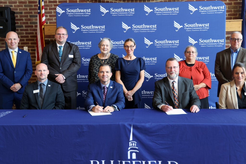 A group surrounding the two presidents signing papers.