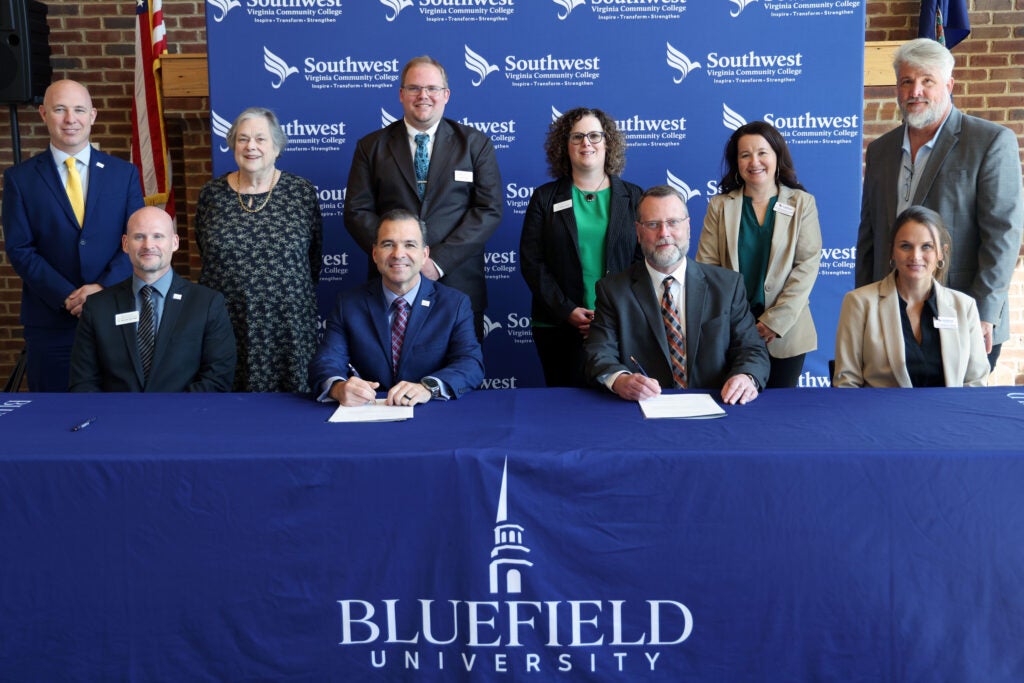 A group surrounding the two presidents signing papers.