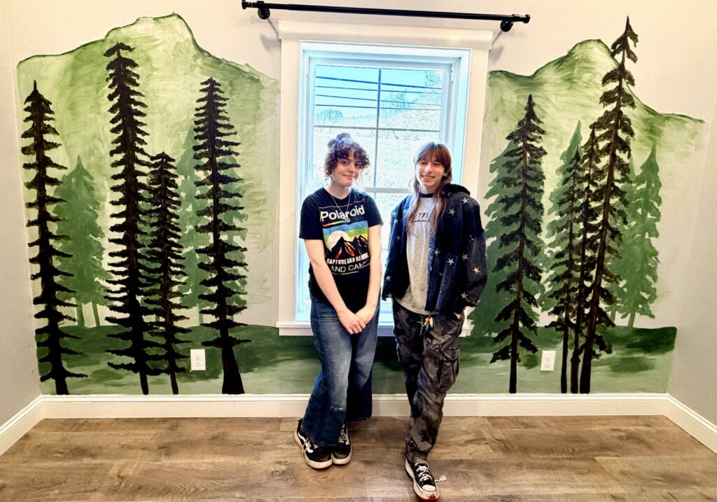 Zouri Metzer and Alan Tuhacek standing in front of a nature mural.