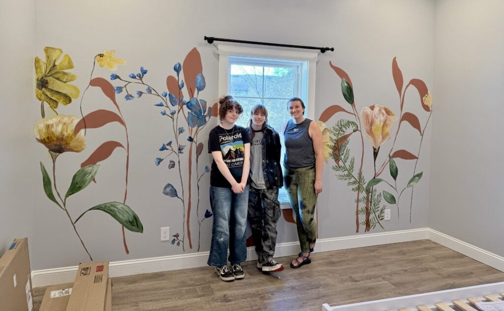 Zouri Metzger, Alan Tuhacek, and Morgan Gilbert standing alongside a flower mural.