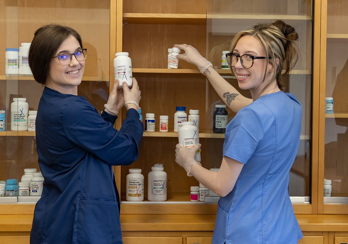 Two female pharmacy tech students holding medication bottles.